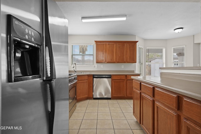 kitchen featuring brown cabinets, light tile patterned floors, stainless steel appliances, light countertops, and a sink