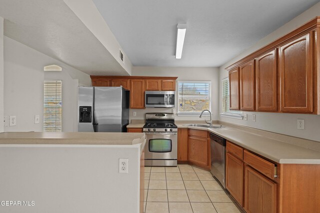 kitchen with light tile patterned floors, a peninsula, stainless steel appliances, light countertops, and a sink