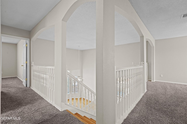 hallway featuring carpet floors, baseboards, visible vents, and a textured ceiling