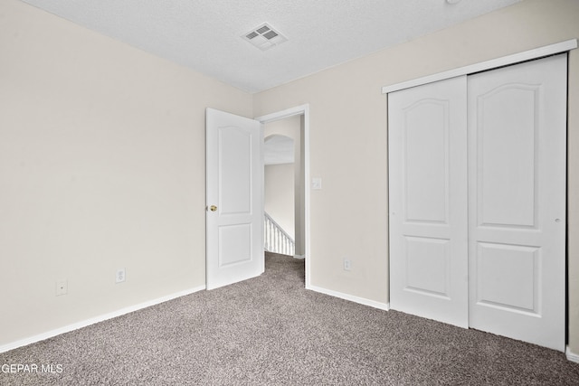 unfurnished bedroom featuring a textured ceiling, carpet flooring, visible vents, baseboards, and a closet