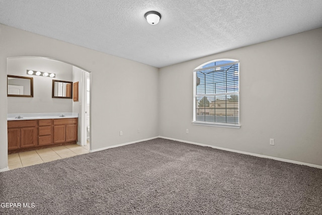 interior space with light tile patterned floors, arched walkways, light colored carpet, ensuite bath, and a textured ceiling