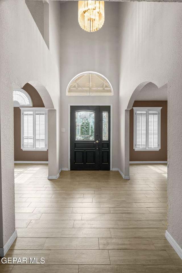 entrance foyer featuring arched walkways, light wood-type flooring, an inviting chandelier, and a healthy amount of sunlight