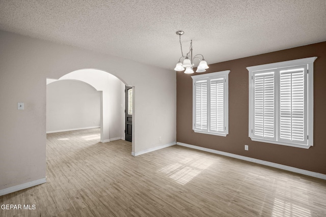 spare room with arched walkways, a textured ceiling, a chandelier, light wood-type flooring, and baseboards