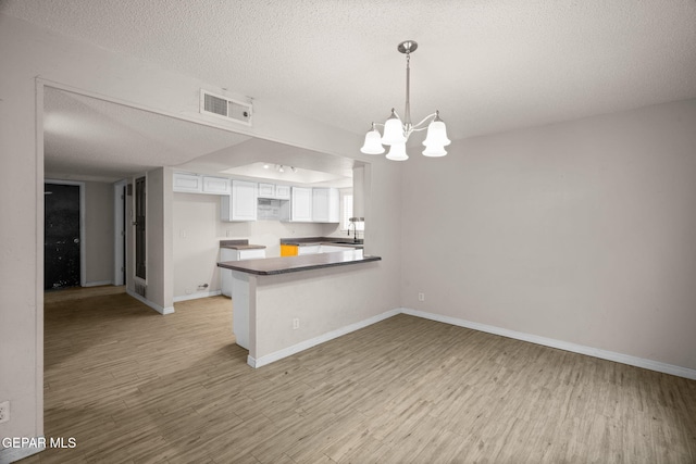 kitchen featuring a peninsula, visible vents, white cabinetry, hanging light fixtures, and dark countertops