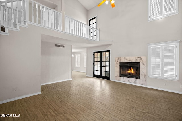 unfurnished living room featuring baseboards, visible vents, ceiling fan, wood finished floors, and a high end fireplace