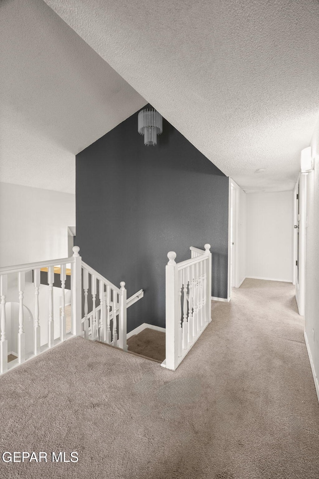 hallway featuring carpet floors, baseboards, a textured ceiling, and an upstairs landing