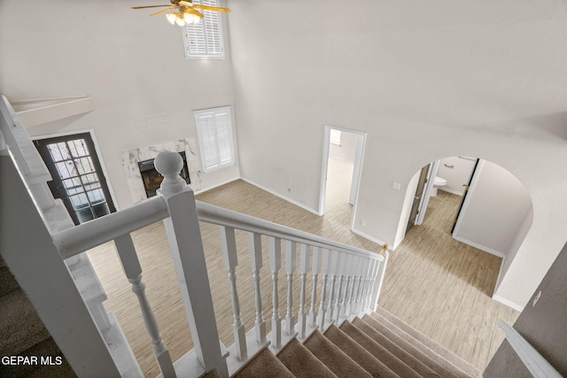 staircase featuring arched walkways, a fireplace, a high ceiling, wood finished floors, and baseboards