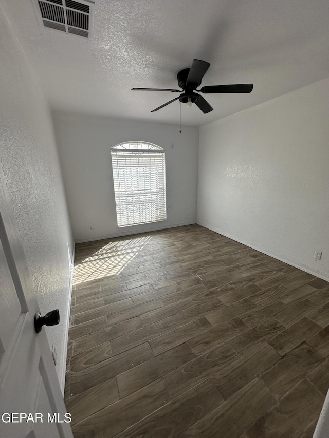 unfurnished room featuring visible vents, a ceiling fan, a textured wall, dark wood-style flooring, and a textured ceiling