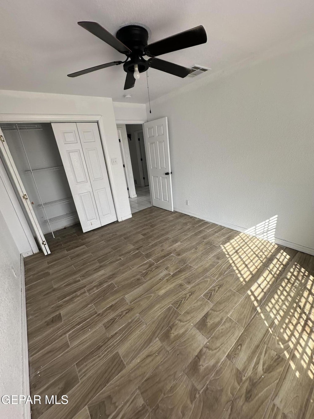 unfurnished bedroom with a closet, dark wood finished floors, visible vents, and a ceiling fan