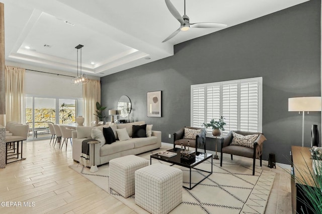 living area with light wood finished floors, ceiling fan, a tray ceiling, and baseboards