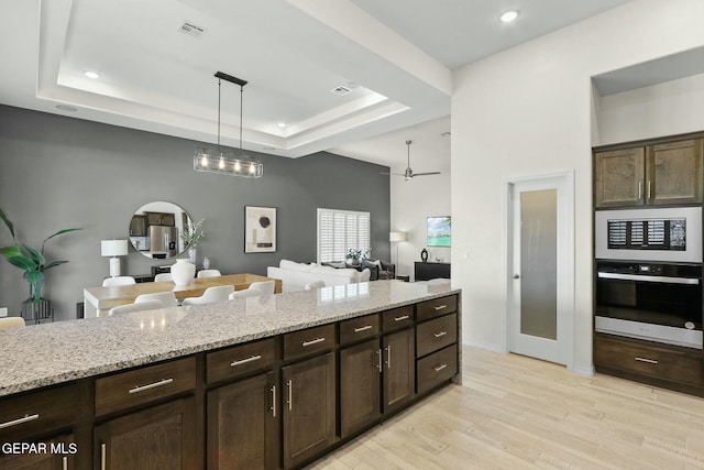 kitchen featuring visible vents, light wood-style flooring, oven, a tray ceiling, and pendant lighting