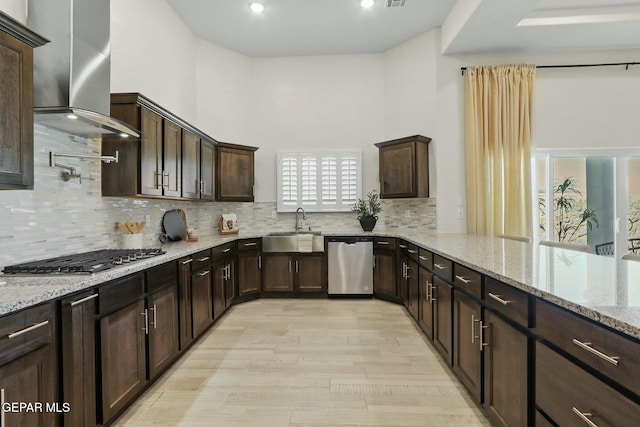 kitchen featuring light stone counters, tasteful backsplash, appliances with stainless steel finishes, a sink, and wall chimney exhaust hood