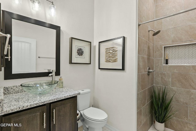 bathroom with toilet, tiled shower, and vanity