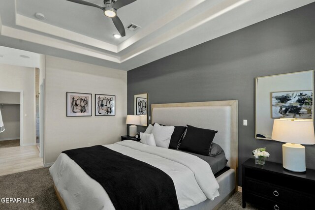 carpeted bedroom featuring baseboards, visible vents, a raised ceiling, and a ceiling fan