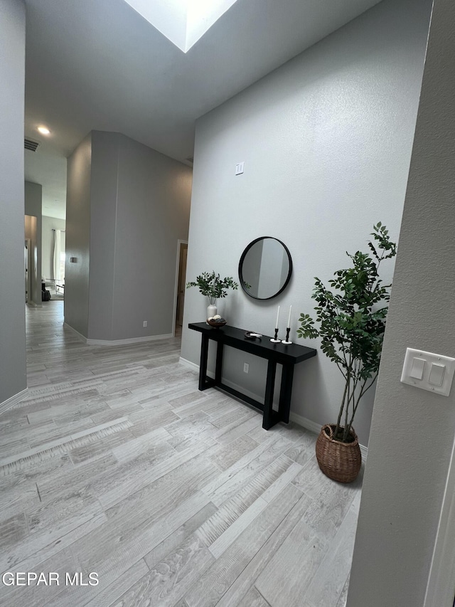 hall with a skylight, visible vents, light wood-style flooring, and baseboards