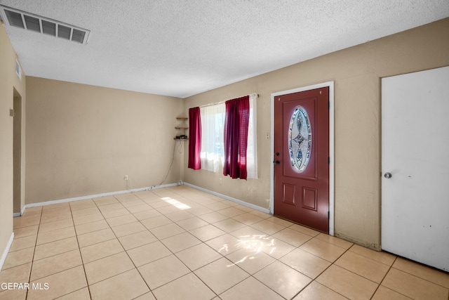 entryway with light tile patterned floors, baseboards, visible vents, and a textured ceiling