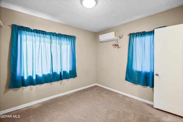 carpeted spare room with a wall unit AC, a textured ceiling, and baseboards