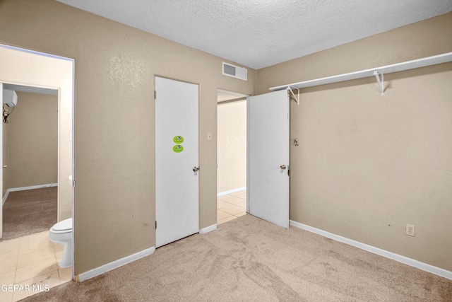 unfurnished bedroom with a textured ceiling, light tile patterned flooring, light carpet, visible vents, and baseboards