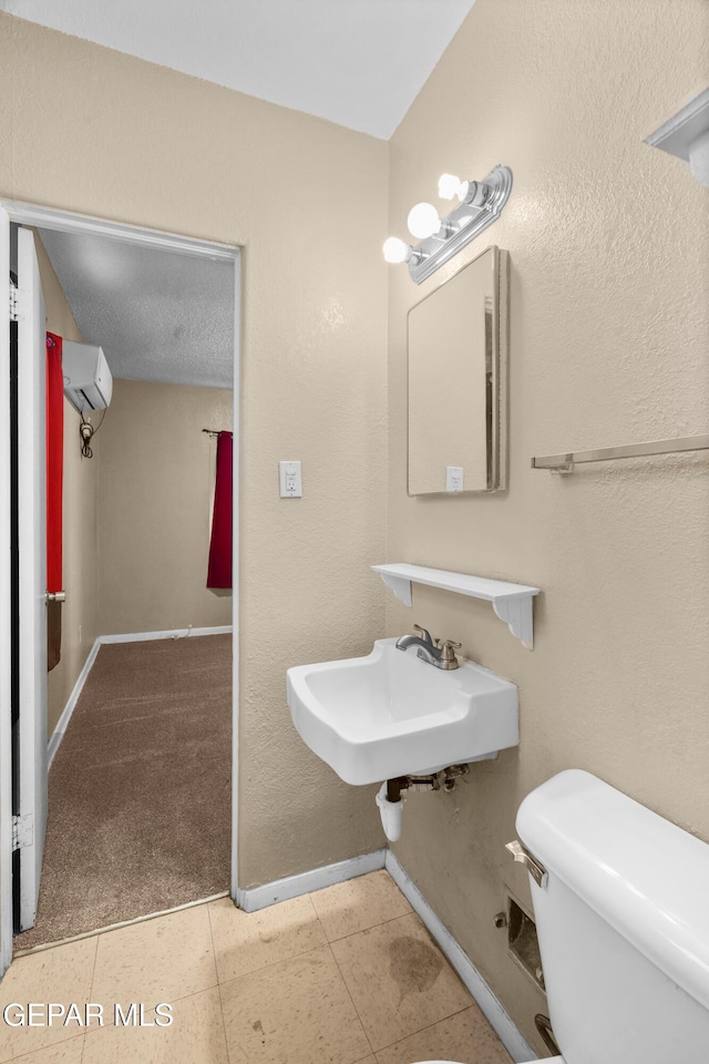 half bathroom featuring baseboards, toilet, tile patterned floors, a wall mounted air conditioner, and a sink