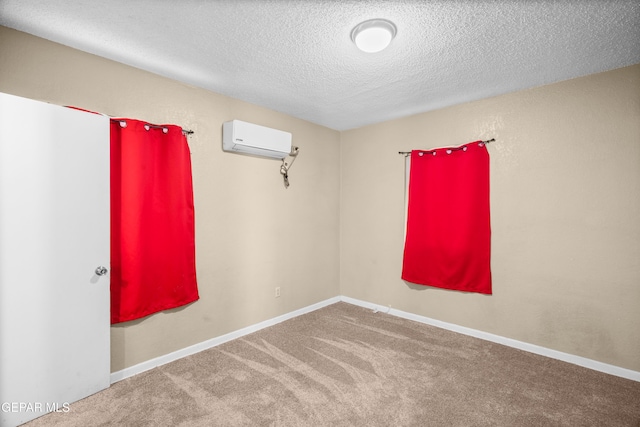 carpeted spare room with a textured ceiling, baseboards, and an AC wall unit