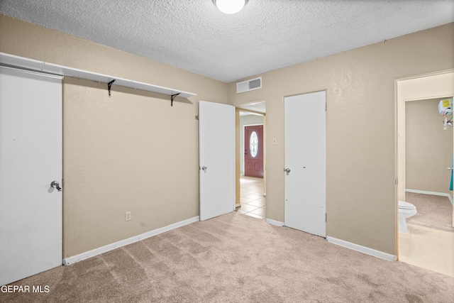 unfurnished bedroom featuring light tile patterned floors, visible vents, connected bathroom, light colored carpet, and a textured ceiling