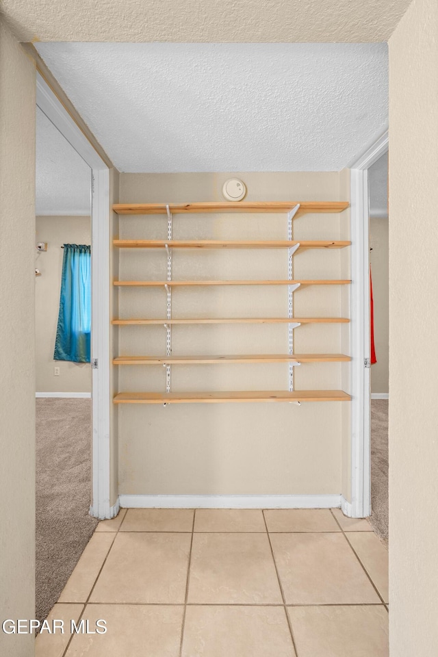 interior space with a textured ceiling, baseboards, carpet flooring, and tile patterned floors