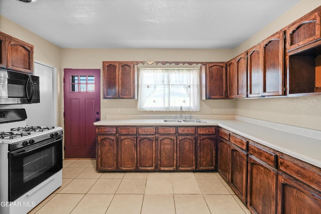 kitchen featuring black microwave, light tile patterned floors, a sink, light countertops, and gas range oven