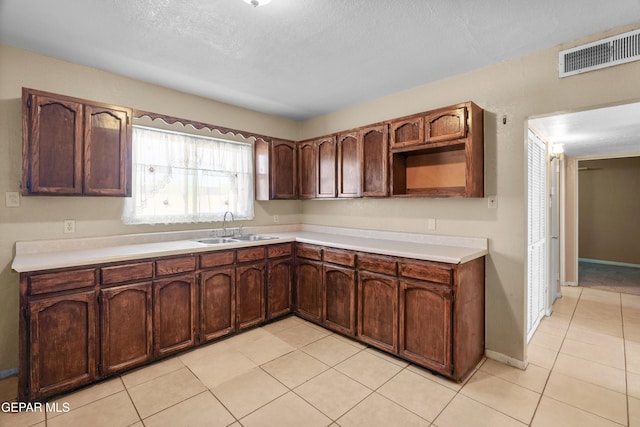 kitchen featuring light tile patterned floors, a sink, visible vents, light countertops, and dark brown cabinets