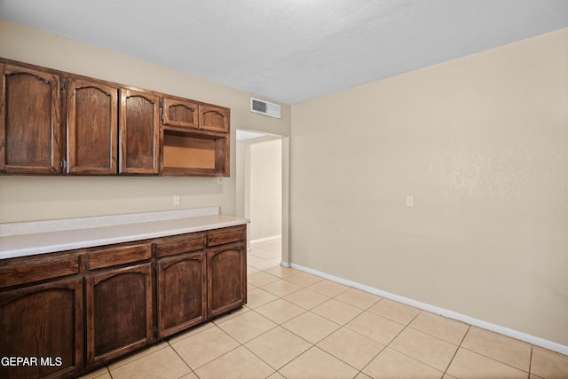 kitchen featuring dark brown cabinetry, light tile patterned floors, baseboards, visible vents, and light countertops