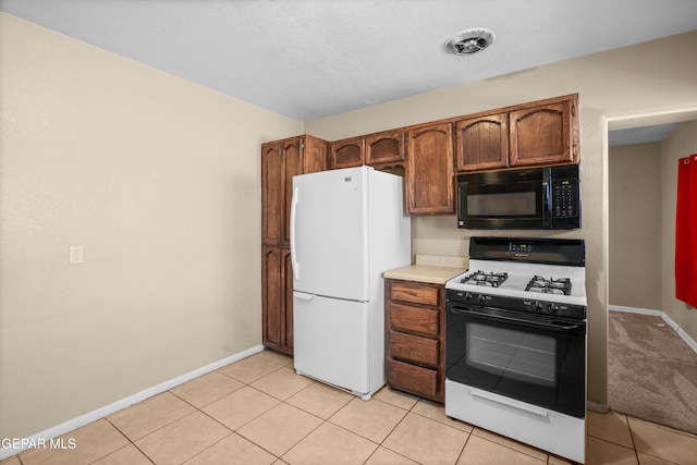 kitchen featuring black microwave, light countertops, freestanding refrigerator, brown cabinets, and range with gas cooktop