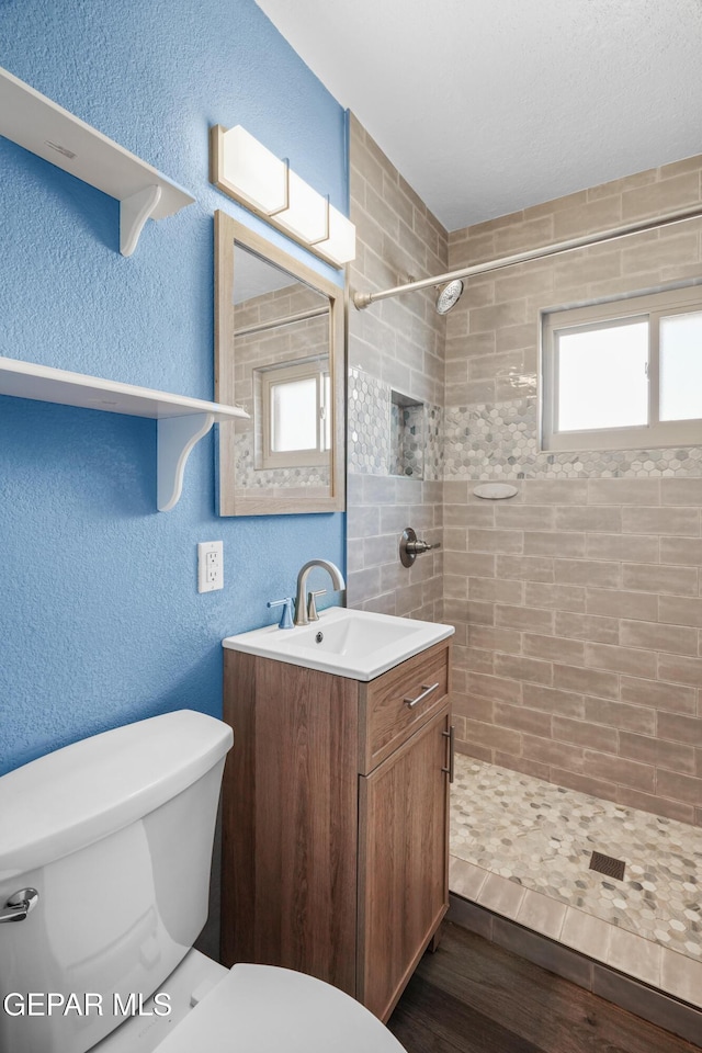 bathroom with a textured wall, toilet, wood finished floors, vanity, and a shower stall