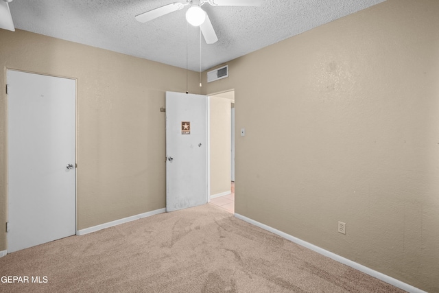 unfurnished bedroom featuring light colored carpet, visible vents, a textured wall, a textured ceiling, and baseboards