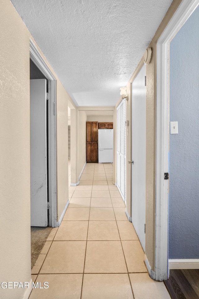 hall with light tile patterned floors, baseboards, a textured ceiling, and a textured wall