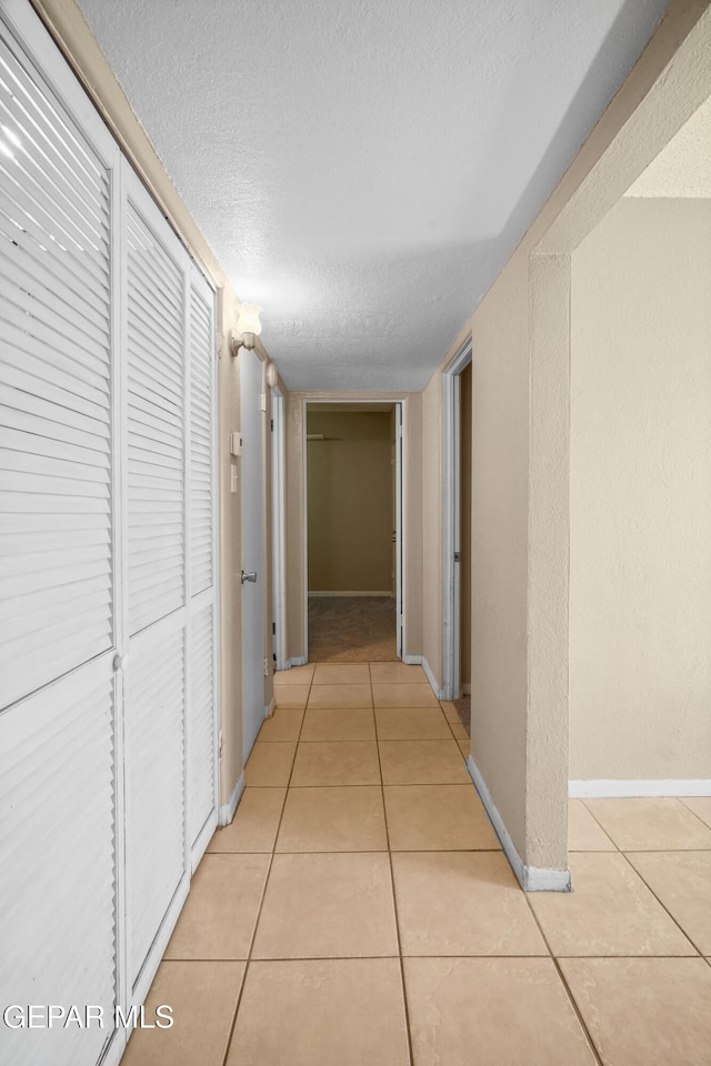 hall featuring light tile patterned flooring, a textured ceiling, and baseboards