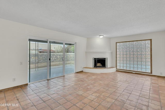 unfurnished living room featuring a fireplace with raised hearth, a textured ceiling, and baseboards