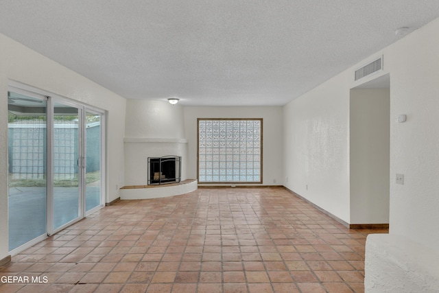 unfurnished living room featuring baseboards, visible vents, a fireplace with raised hearth, a textured wall, and a textured ceiling