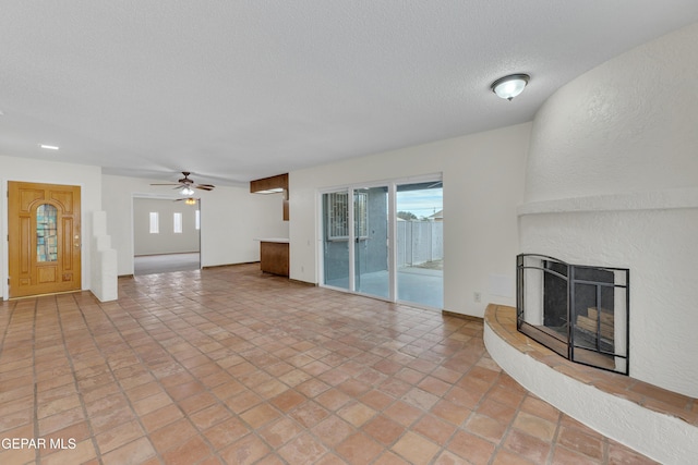 unfurnished living room with a large fireplace, a textured wall, a textured ceiling, and a ceiling fan