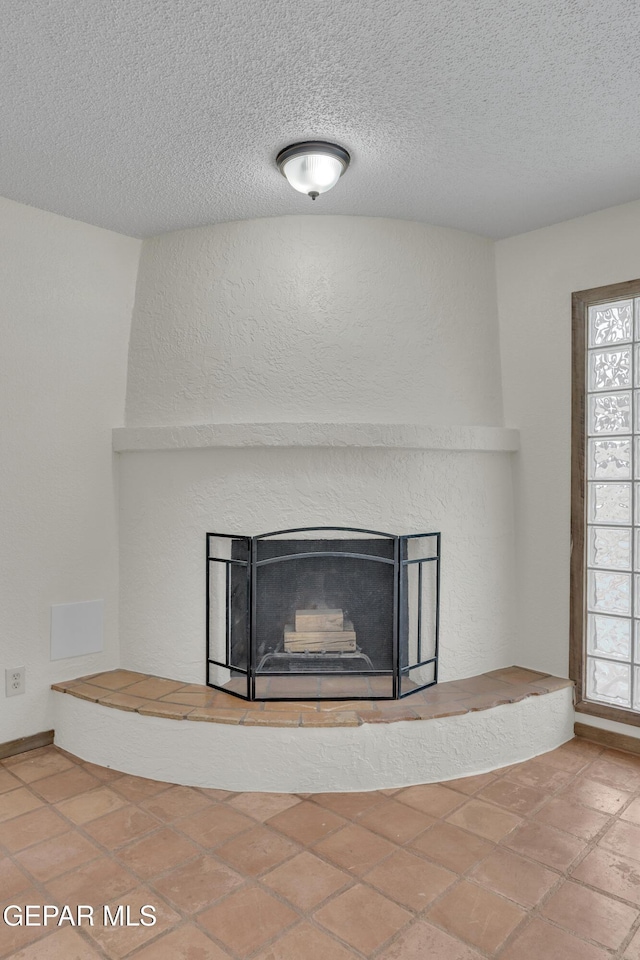 room details with a fireplace with raised hearth, a textured wall, and a textured ceiling