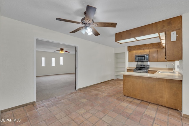 kitchen featuring light countertops, appliances with stainless steel finishes, open floor plan, a sink, and a peninsula