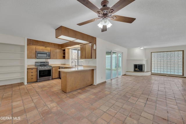 kitchen featuring appliances with stainless steel finishes, open floor plan, a peninsula, light countertops, and open shelves