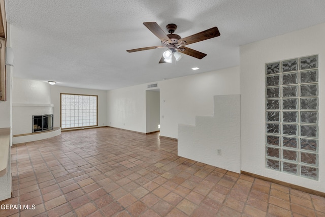 unfurnished living room with a textured ceiling, visible vents, a fireplace with raised hearth, and a ceiling fan