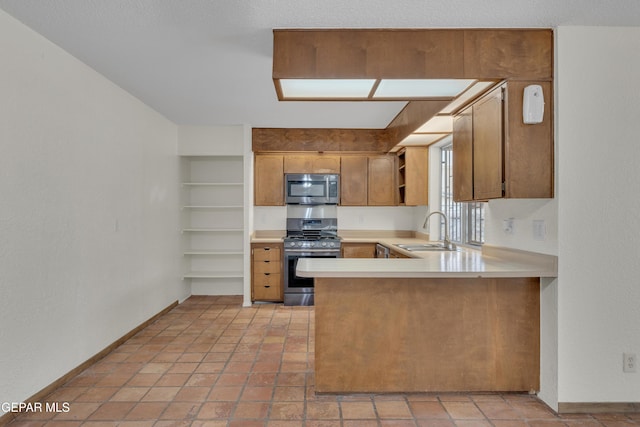 kitchen with brown cabinetry, appliances with stainless steel finishes, a peninsula, light countertops, and a sink