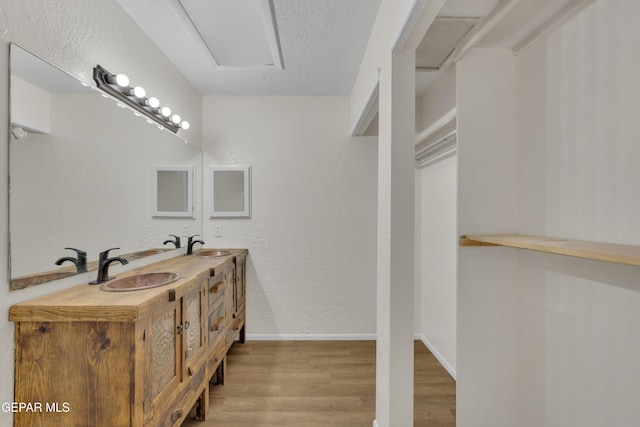 full bathroom featuring double vanity, baseboards, wood finished floors, a textured ceiling, and a sink