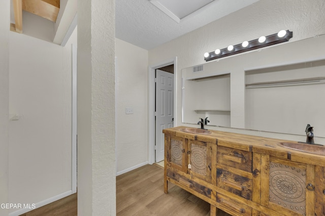 full bathroom with a sink, a textured ceiling, and wood finished floors