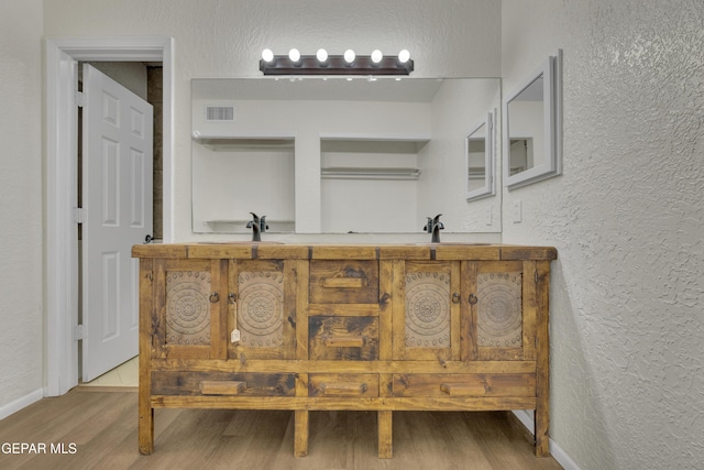 bathroom featuring visible vents, a textured wall, a sink, and wood finished floors