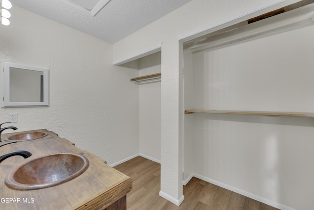 full bath featuring a sink, a textured ceiling, baseboards, and wood finished floors