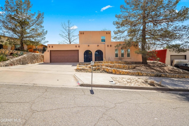 pueblo-style home featuring concrete driveway, an attached garage, and stucco siding