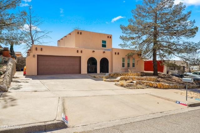 adobe home with concrete driveway, an attached garage, and stucco siding