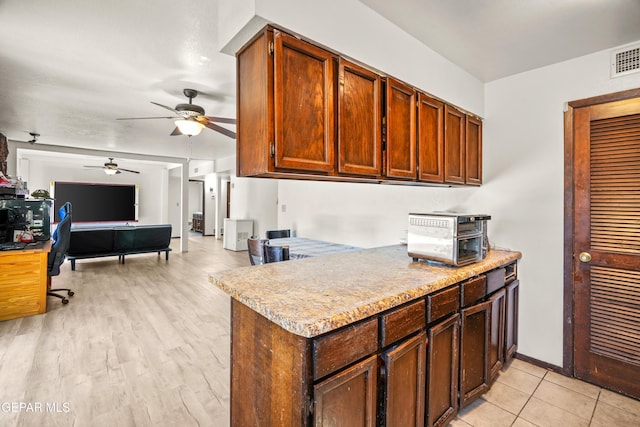 kitchen featuring ceiling fan, light wood-style flooring, baseboards, open floor plan, and light countertops