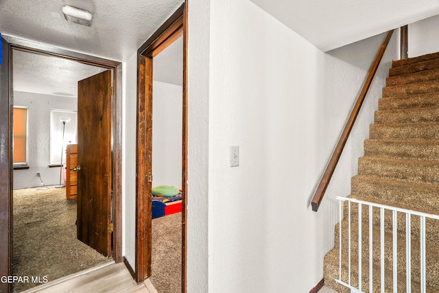 hallway featuring a textured ceiling, light wood finished floors, light carpet, and stairs